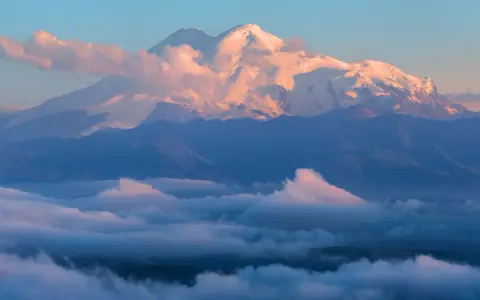 Elbrus, najwyższy szczyt Kaukazu, lśni w blasku wschodzącego słońca, otoczony morzem chmur.