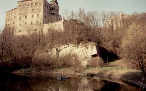 Zamek na skale nad wodą, otoczony drzewami. To krajobraz Ojcowskiego Parku Narodowego, najmniejszego parku narodowego w Polsce.