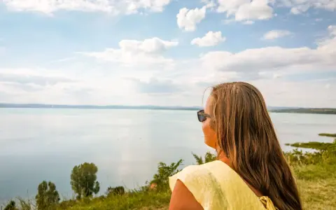 Kobieta w żółtej bluzce podziwia rozległe jezioro Balaton.