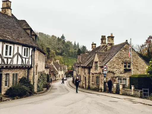 Kamienna uliczka w Cotswolds z tradycyjnymi domami i ludźmi spacerującymi po drodze.