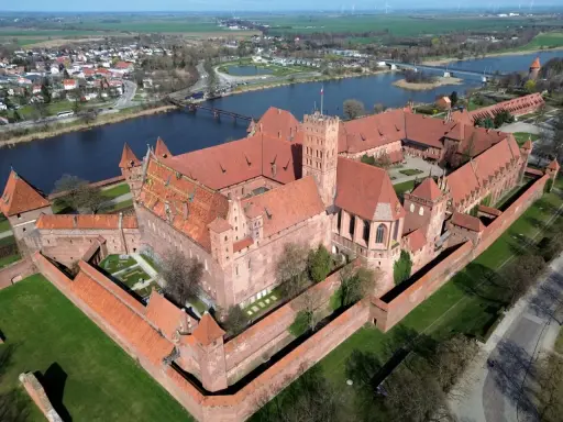 Malbork, największy zamek w Europie, rozciąga się wzdłuż rzeki, otoczony murami obronnymi i zielonymi dziedzińcami.