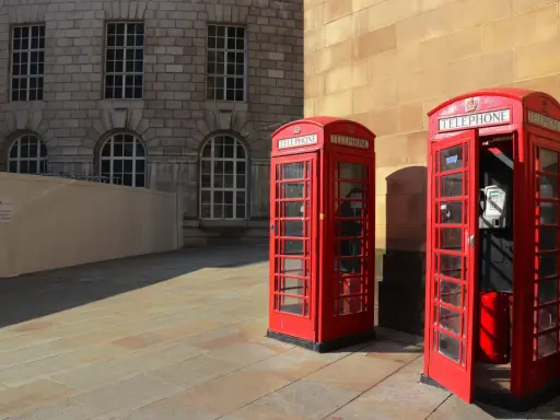 Klasyczne czerwone budki telefoniczne na brukowanym placu, w tle kamienna fasada budynku. Manchester miasto.