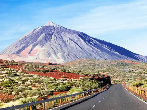 Droga prowadząca do wulkanu Teide na Teneryfie, otoczona suchą roślinnością i czerwonymi skałami.