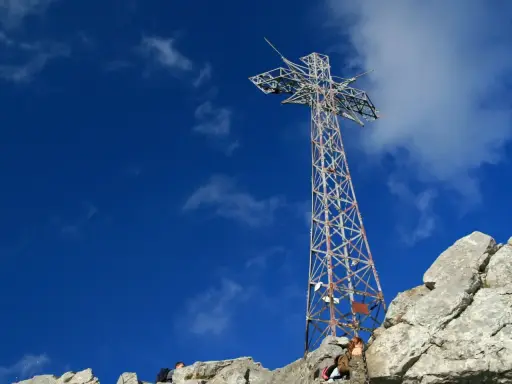 Metalowy krzyż na skalistym szczycie Giewontu pod błękitnym niebem z chmurami.