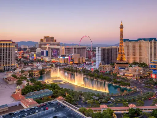 Las Vegas, miasto hazardu w USA, nocą. Widać fontanny, wieżę Eiffla i diabelski młyn.