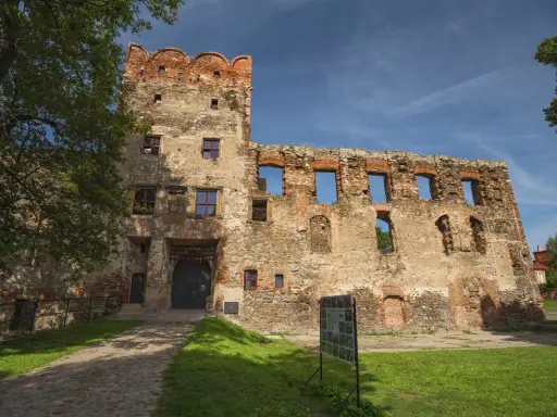 Zamek w Ząbkowicach Śląskich, ruiny z ceglaną wieżą i bramą, otoczone zielenią i błękitnym niebem.