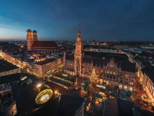 Nocny jarmark bożonarodzeniowy w Monachium. Rynek z oświetlonymi straganami i choinką, w tle Frauenkirche i Nowy Ratusz.
