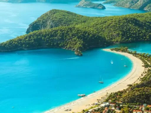 Idealne miejsce, gdzie jechać w niedzielę: turkusowa zatoka, piaszczysta plaża, zielone wzgórza i żaglówki.