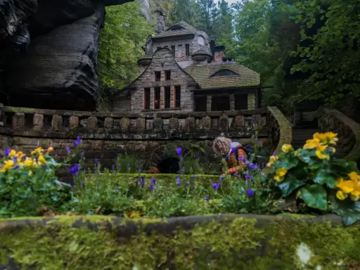 Kamienny domek w sercu Szwajcarii Czeskiej, otoczony bujną zielenią i kwitnącymi kwiatami.