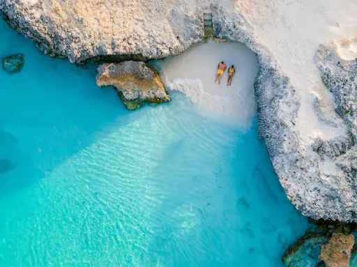 Para relaksuje się na ukrytej plaży na wyspie Aruba, otoczonej turkusową wodą i skalistymi klifami.