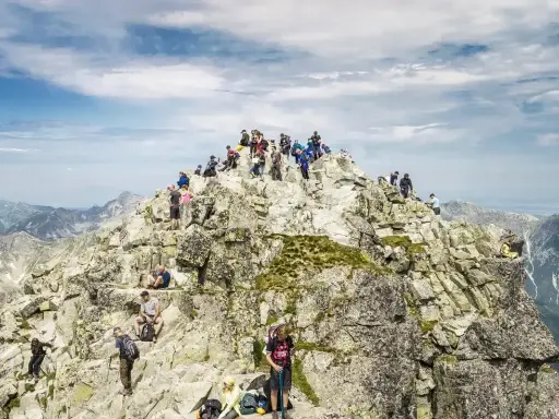 Tłum turystów na szczycie Rysów od strony polskiej. Wspinacze odpoczywają na skalistym grzbiecie, podziwiając panoramę Tatr.