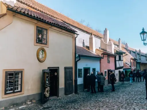 Urokliwa, brukowana złota uliczka w Pradze, z kolorowymi domkami i turystami spacerującymi pośród nich.