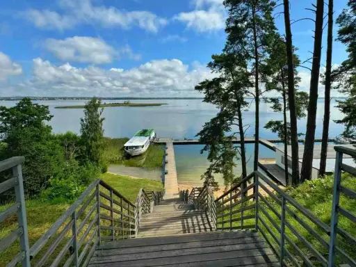 Mazury, gdzie jechać? Widok na jezioro z pomostem i statkiem. Drewniane schody prowadzą do wody, idealne miejsce na wypoczynek.