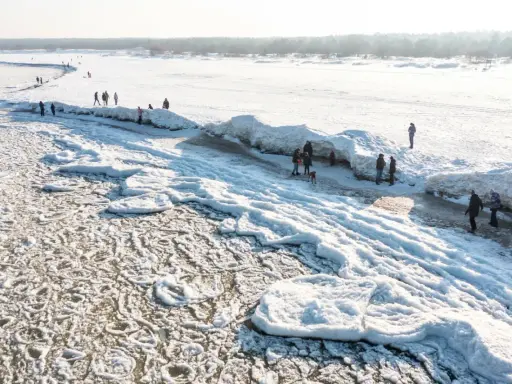 Ludzie spacerują po zamarzniętej plaży z lodowymi formacjami przypominającymi góry.