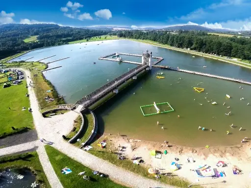 Letnia rekreacja nad zalewem, gdzie czarna góra stanowi malownicze tło dla wodnych atrakcji i wypoczynku na plaży.