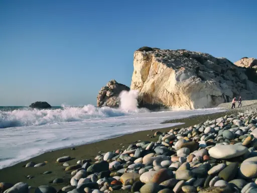 Kamienista plaża na wyspie Afrodyty, gdzie fale rozbijają się o skaliste klify.