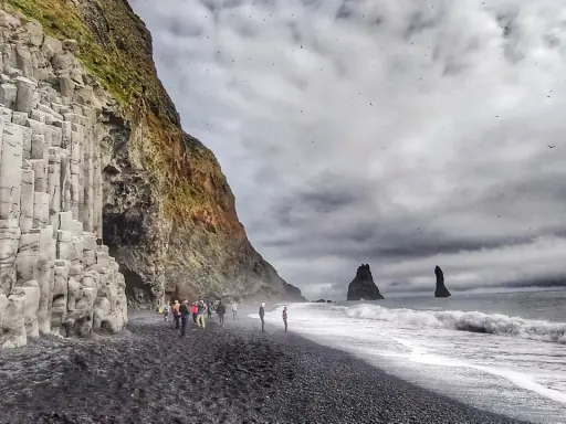 Skały bazaltowe na plaży Reynisfjara, czarny piasek, fale i skalne iglice w morzu.