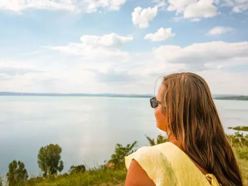 Kobieta w żółtej bluzce podziwia rozległe jezioro Balaton.