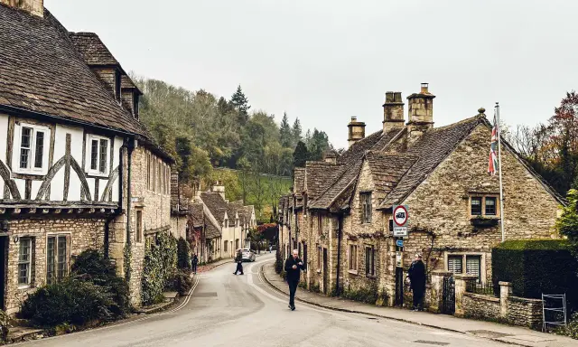 Kamienna uliczka w Cotswolds z tradycyjnymi domami i ludźmi spacerującymi po drodze.