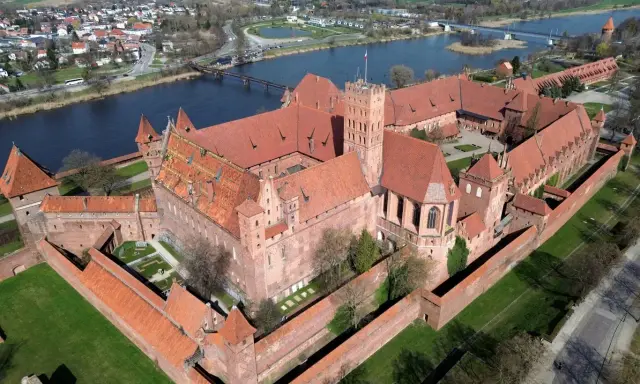 Malbork, największy zamek w Europie, rozciąga się wzdłuż rzeki, otoczony murami obronnymi i zielonymi dziedzińcami.