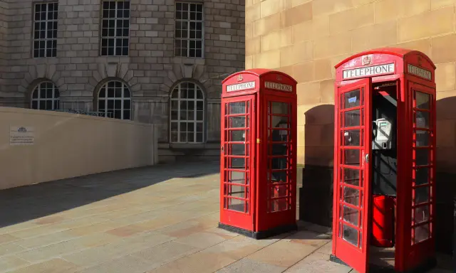 Klasyczne czerwone budki telefoniczne na brukowanym placu, w tle kamienna fasada budynku. Manchester miasto.