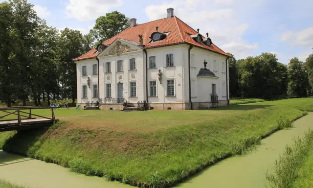 Pałac w Choroszczy otoczony fosą i zielenią, z drewnianym mostkiem prowadzącym do wejścia.