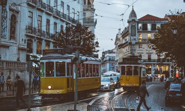 Lisbona, Portugalia. Żółte tramwaje na brukowanej ulicy, ludzie i samochody. Ceny w Portugalii mogą być różne, ale widok wart jest każdej ceny.