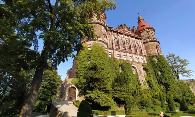 Imponujący zamek porośnięty bluszczem, z czerwoną wieżą i zadbanym ogrodem. Sprawdź zamek książ cennik przed wizytą.