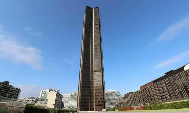 Wieżowiec Montparnasse w Paryżu, dominujący nad innymi budynkami, na tle błękitnego nieba z chmurami.