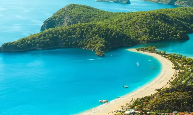 Idealne miejsce, gdzie jechać w niedzielę: turkusowa zatoka, piaszczysta plaża, zielone wzgórza i żaglówki.