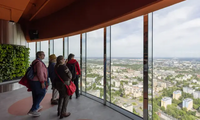 Grupa turystów podziwia panoramę miasta z tarasu widokowego najwyższego budynku we Wrocławiu.