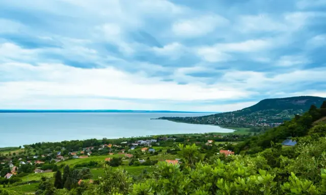Widok na Balaton z góry, z zielonymi wzgórzami i domkami. W oddali widać jezioro i plażę.