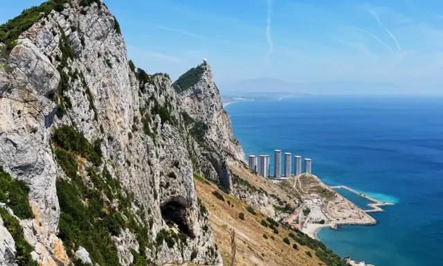 Gibraltar, brytyjskie terytorium na półwyspie iberyjskim, z górującą skałą, jaskinią i nowoczesnymi budynkami nad błękitnym morzem.