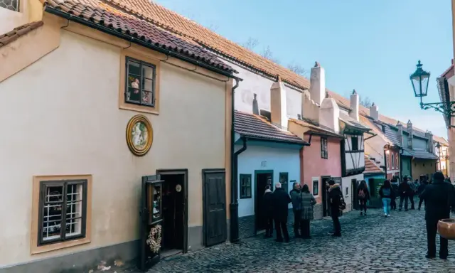 Urokliwa, brukowana złota uliczka w Pradze, z kolorowymi domkami i turystami spacerującymi pośród nich.