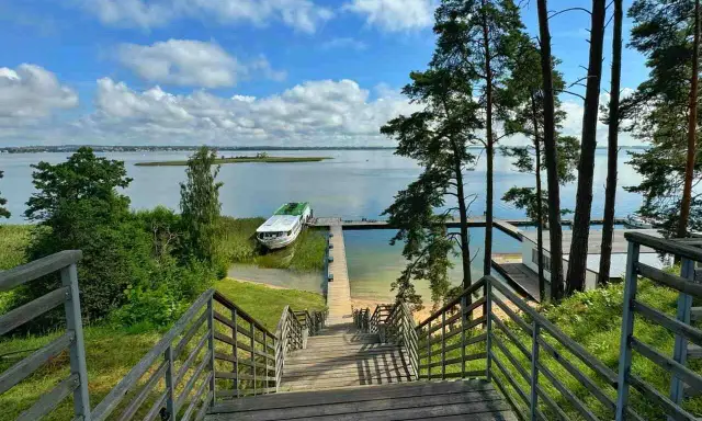 Mazury, gdzie jechać? Widok na jezioro z pomostem i statkiem. Drewniane schody prowadzą do wody, idealne miejsce na wypoczynek.