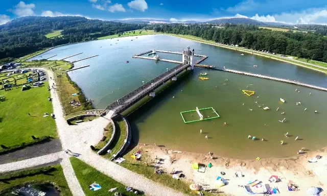 Letnia rekreacja nad zalewem, gdzie czarna góra stanowi malownicze tło dla wodnych atrakcji i wypoczynku na plaży.
