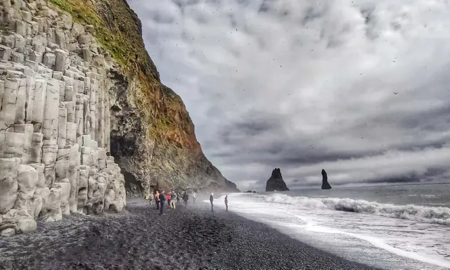 Skały bazaltowe na plaży Reynisfjara, czarny piasek, fale i skalne iglice w morzu.