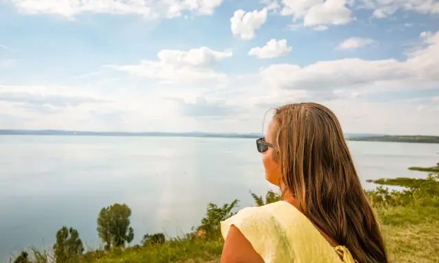 Kobieta w żółtej bluzce podziwia rozległe jezioro Balaton.