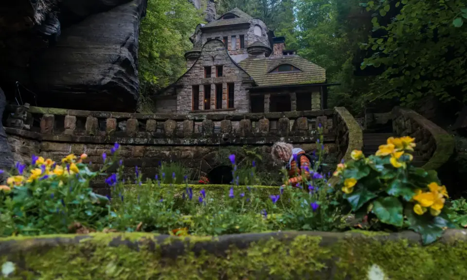 Kamienny domek w sercu Szwajcarii Czeskiej, otoczony bujną zielenią i kwitnącymi kwiatami.