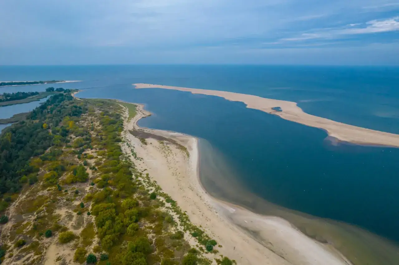 Piaszczysta wyspa na Bałtyku, otoczona turkusową wodą, z zielonymi zaroślami i piaszczystymi plażami.