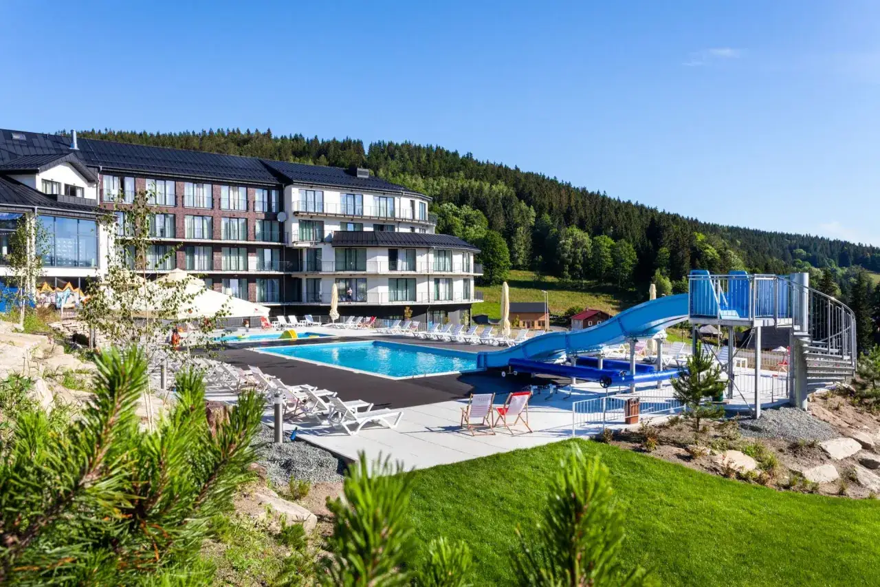 Nowoczesny hotel z basenem i zjeżdżalnią wodną, otoczony zielenią. Idealne miejsce na wypoczynek i odkrywanie czarna góra atrakcje.