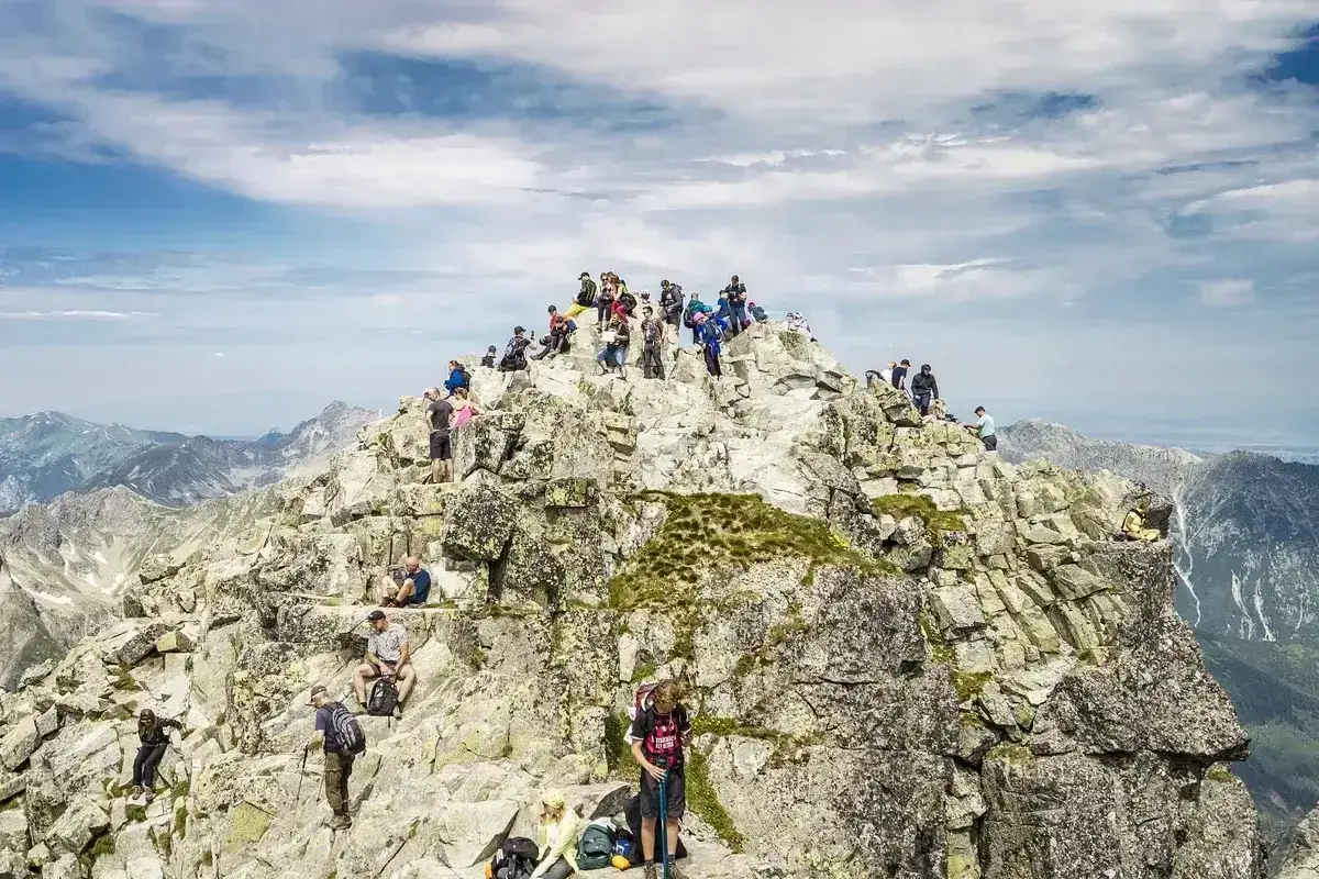Tłum turystów na skalistym szczycie, zdobywający jedne z najwyższych szczytów w Polsce. Widok na Tatry.