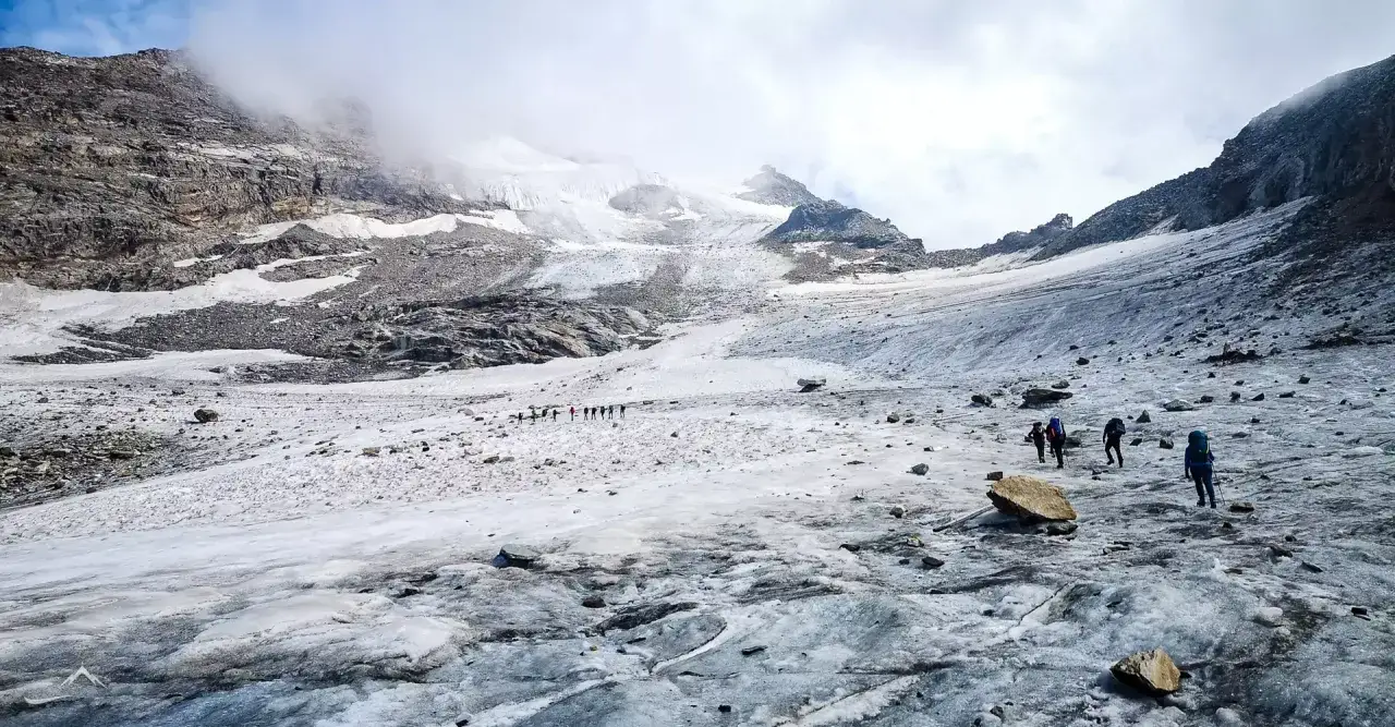 Grupa turystów wędruje po lodowcu w kierunku majestatycznego masywu Monte Rosa.