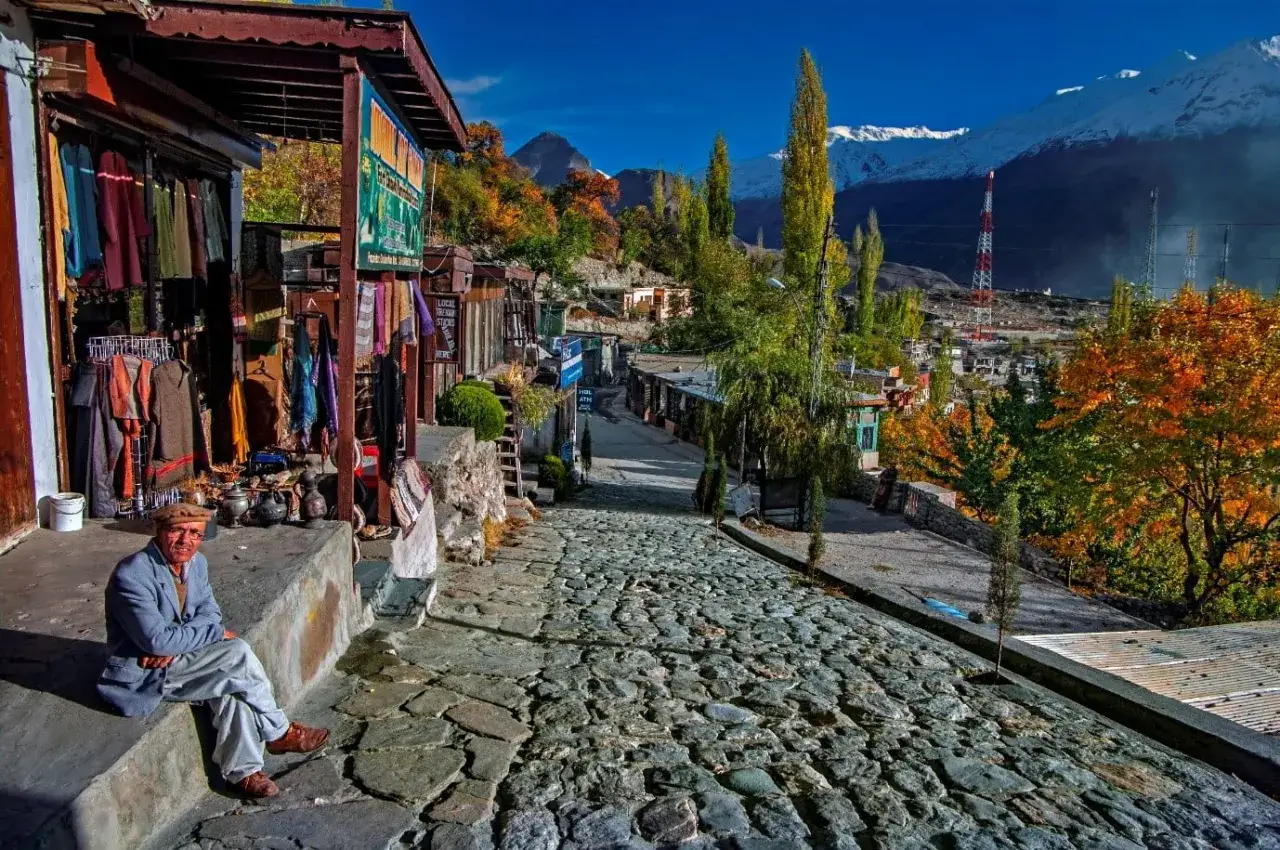 Mężczyzna w czapce siedzi przed sklepem z ubraniami w malowniczej dolinie Hunza.