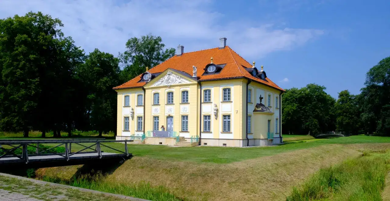 Pałac Branickich w Choroszczy, żółty z pomarańczowym dachem, otoczony zielenią i fosą.